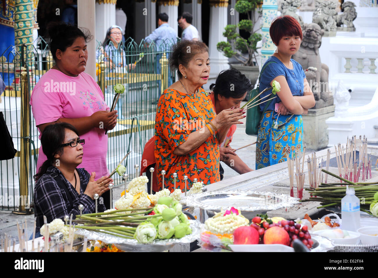 Thai women praying, holding lotus flowers and incense sticks - Wat Phra Kaeo Grand Palace, Bangkok Thailand Stock Photo