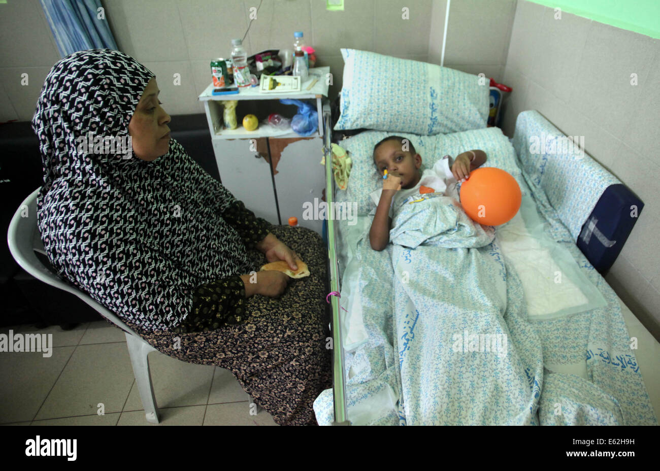 Jerusalem, Jerusalem, Palestinian Territory. 12th Aug, 2014. Mother of Khaled Abu Mrahil, a 6-year-old Palestinian boy, who medics said was wounded during the Israeli offensive on Gaza Strip, sits near her son as he lies on a bed at al-Maqased hospital in Jerusalem on August 12, 2014. Talks to end a month-long war between Israel and Gaza militants are ''difficult'', Palestinian delegates said on Tuesday, while an Israeli official said no progress had been made so far. As a 72-hour ceasefire held for a second day, Palestinian negotiators Credit:  Saeed Qaq/APA Images/ZUMA Wire/Alamy Live News Stock Photo