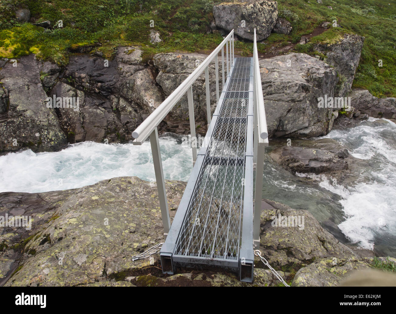 Modern footbridge crossing river with rushing, fresh water cascading, summer mountain scene, Jotunheimen Norway Stock Photo
