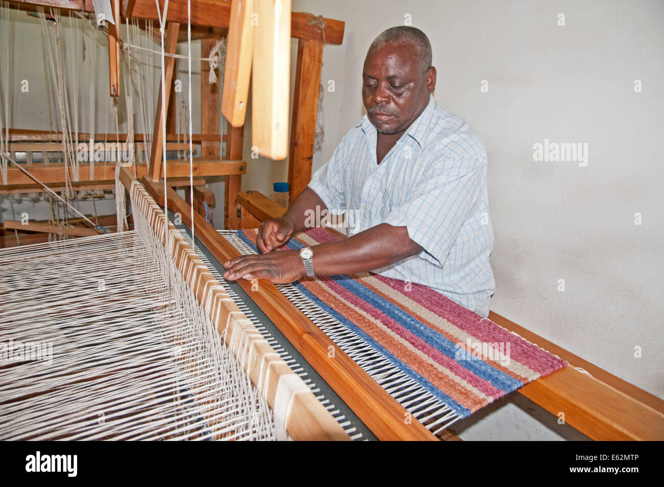 Black African man weaving a woollen rug on loom at Elmentieta Weavers on Lake Road Naivasha Kenya Africa  LOOM WEAVE WEAVER RUG Stock Photo