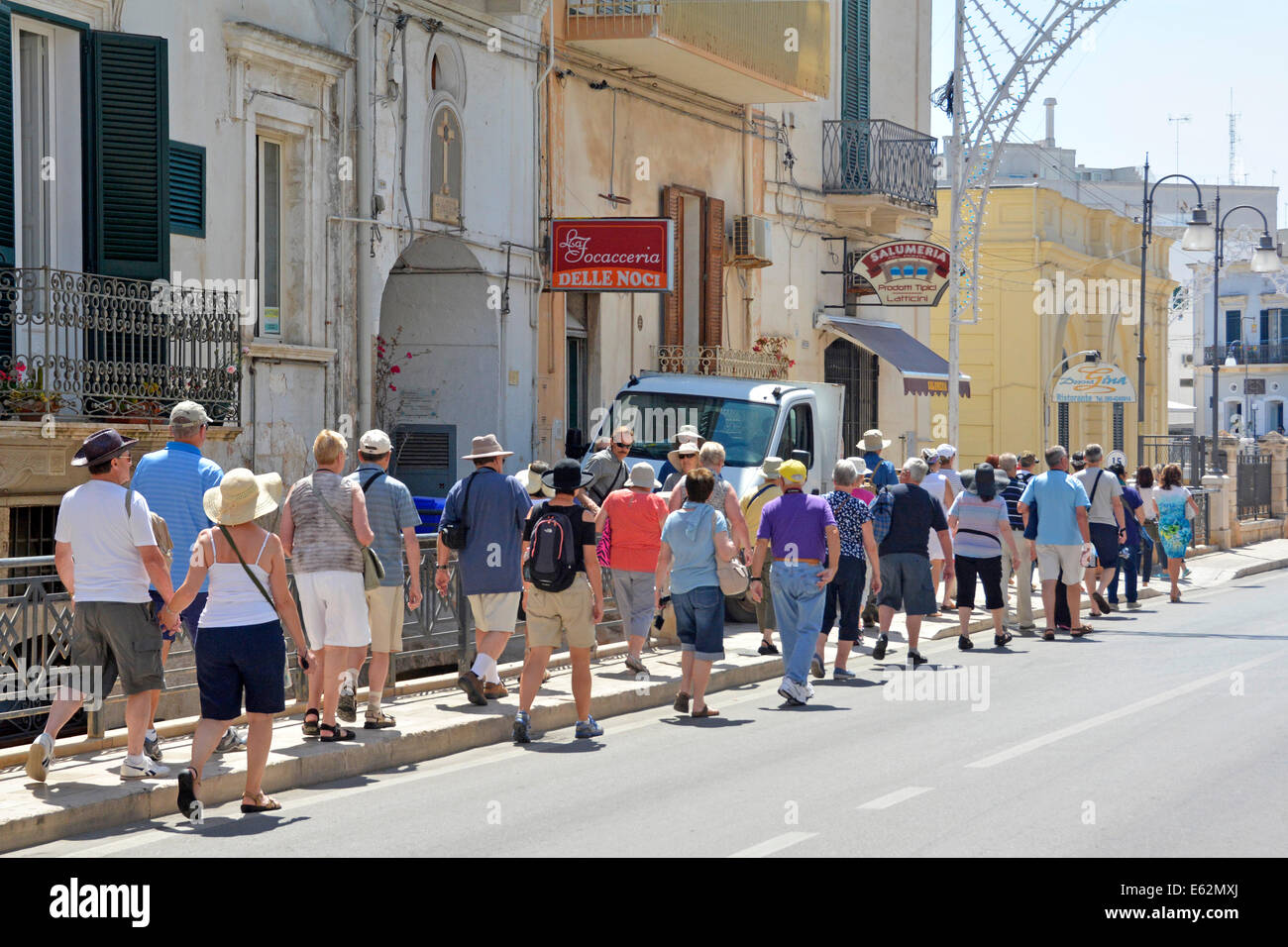 Back view group holiday tourists people from visiting coach party walking in line on street in Polignano a Mare Province of Bari Apulia Puglia Italy Stock Photo