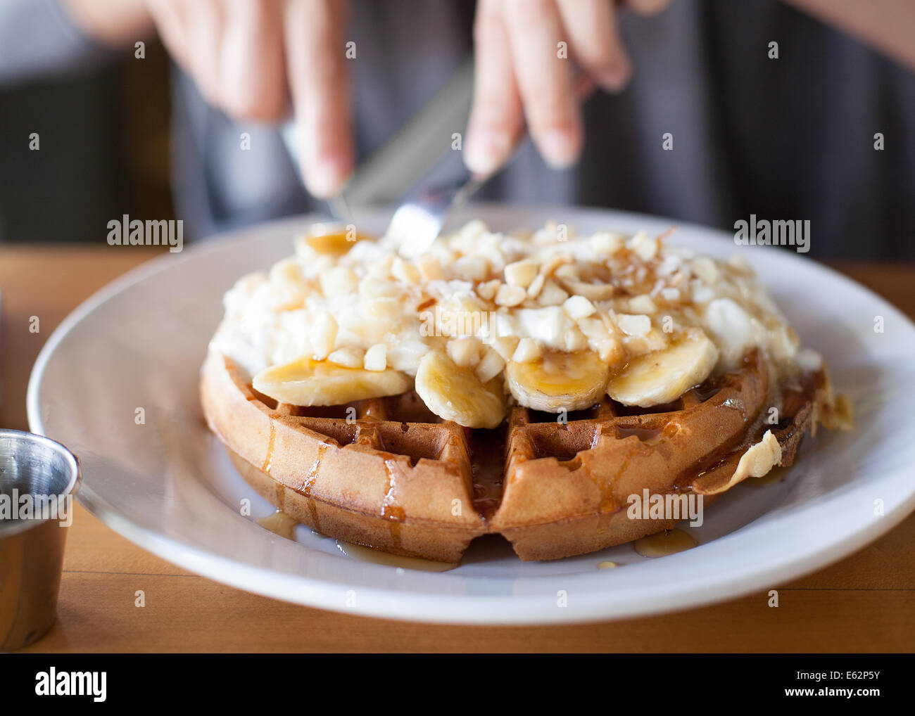 woman cutting up a banana macadamia nut waffle Stock Photo