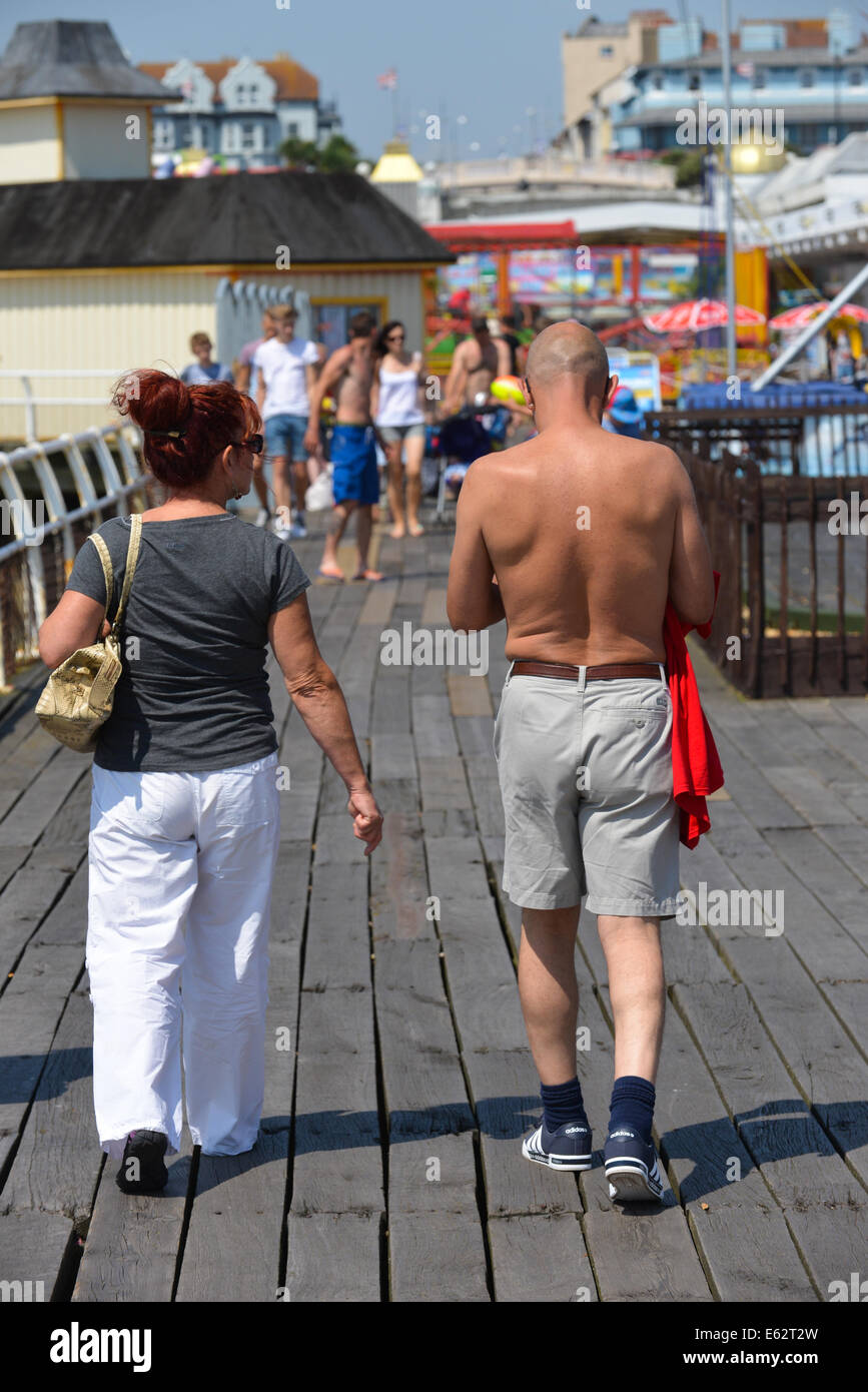 Two people couple man not wearing shirt tanned woman walking along Clacton Pier summer sunshine hot English holiday Stock Photo