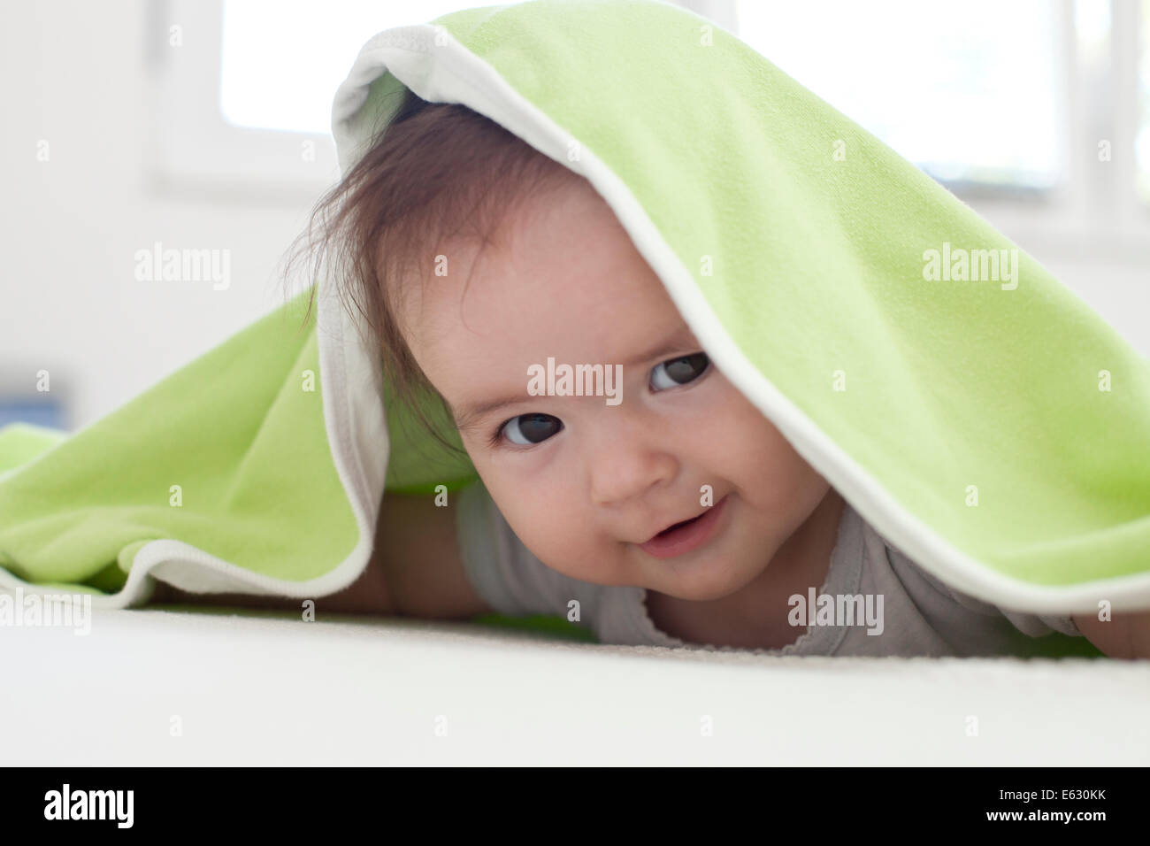 Baby girl is hiding under the white and green blanket Stock Photo Alamy