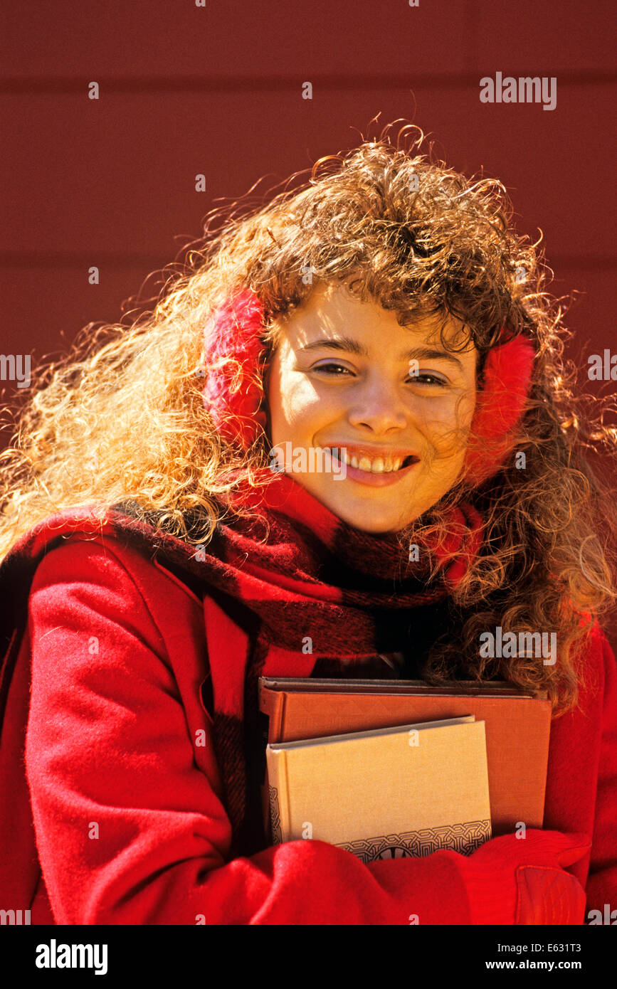 1980s TEENAGE GIRL WEARING EARMUFFS AND CARRYING BOOKS LOOKING AT CAMERA Stock Photo