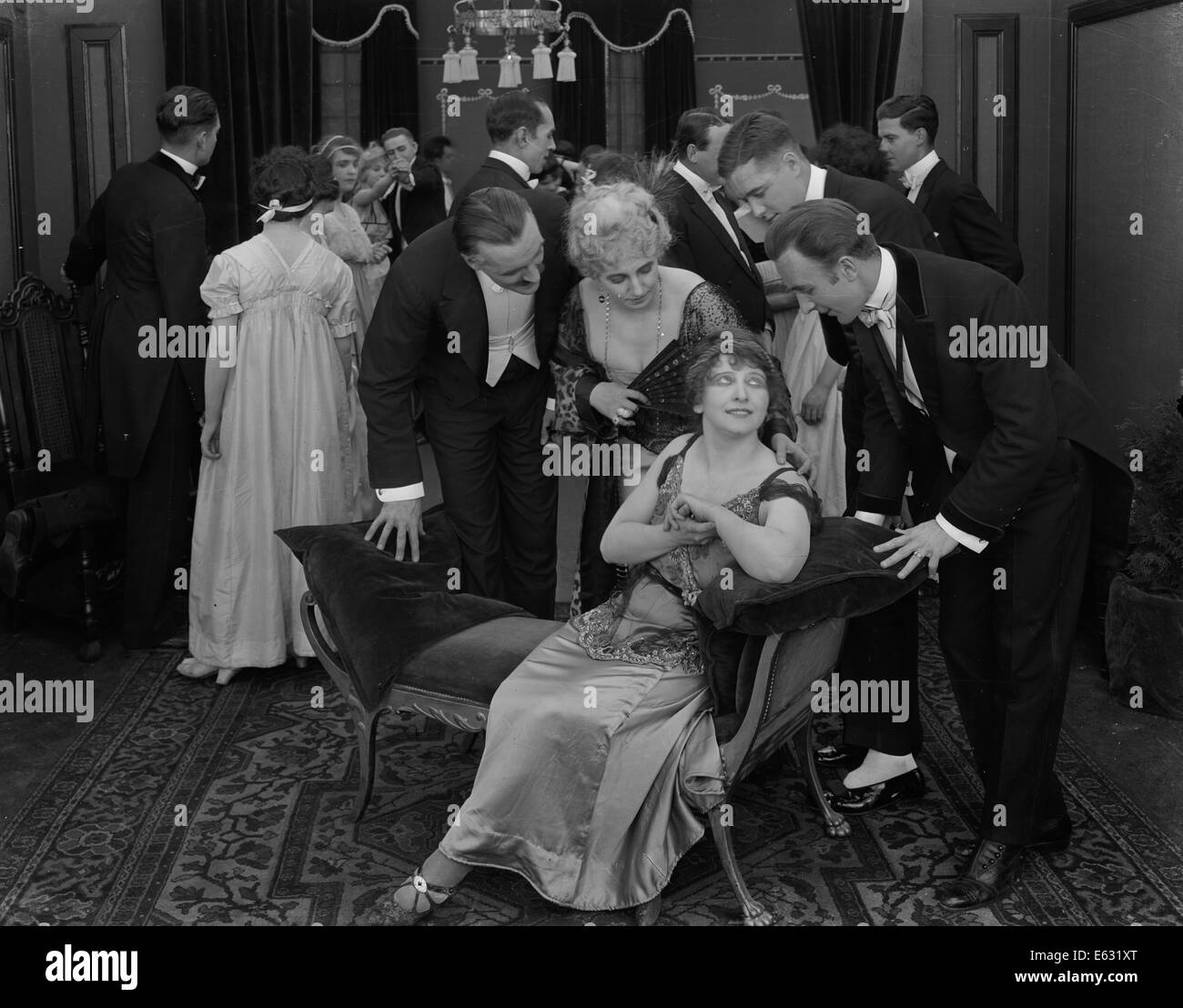 1900s 1910s 1920s SMALL GROUP ATTENDING TO SEATED WOMAN AMIDST FORMAL SOCIETY PARTY SILENT MOVIE STILL Stock Photo
