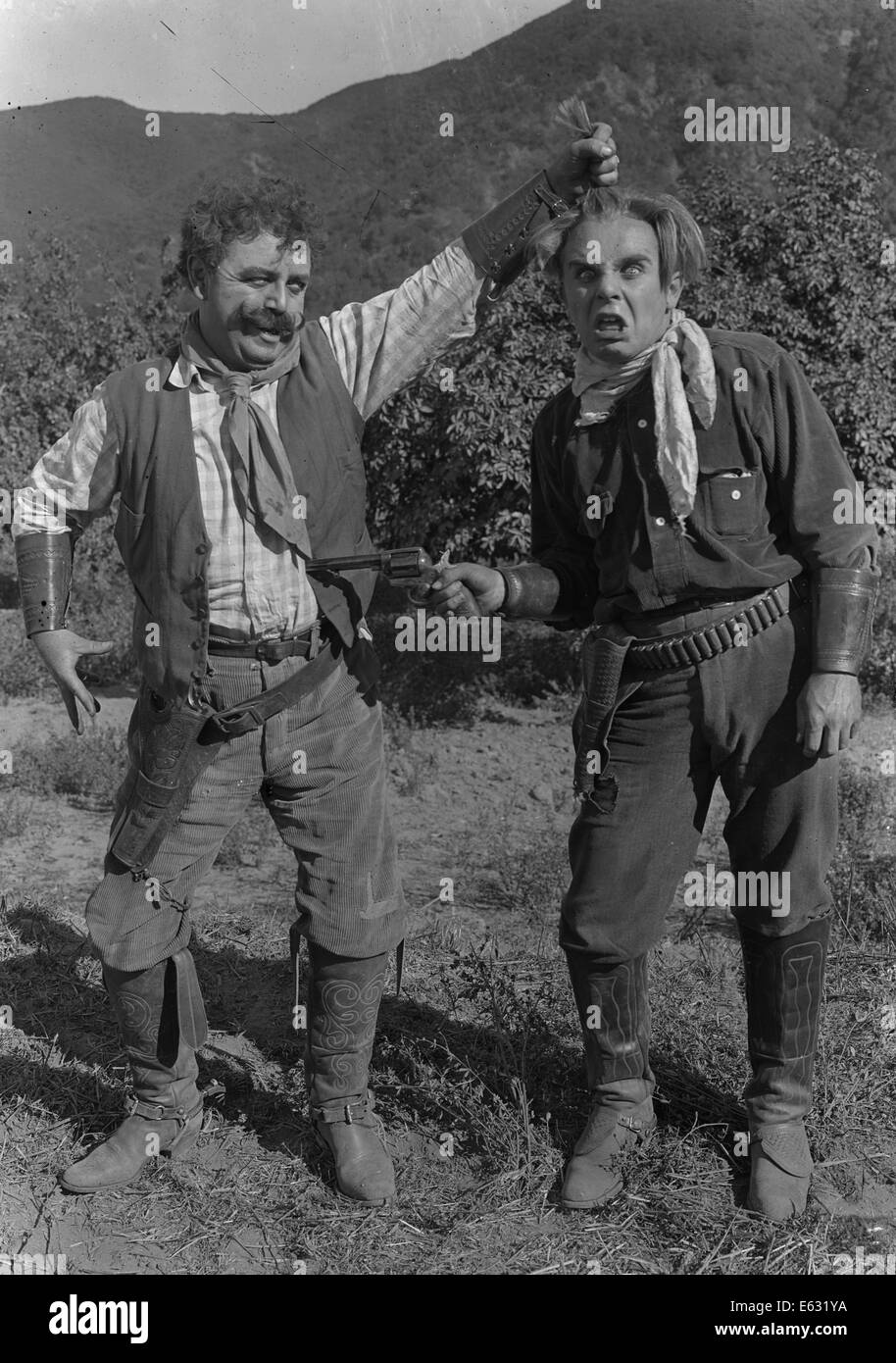 1910s TWO GOOFY COWBOYS ONE POINTING GUN AT BELLY OF THE OTHER PULLING HIS HAIR SILENT MOVIE STILL Stock Photo