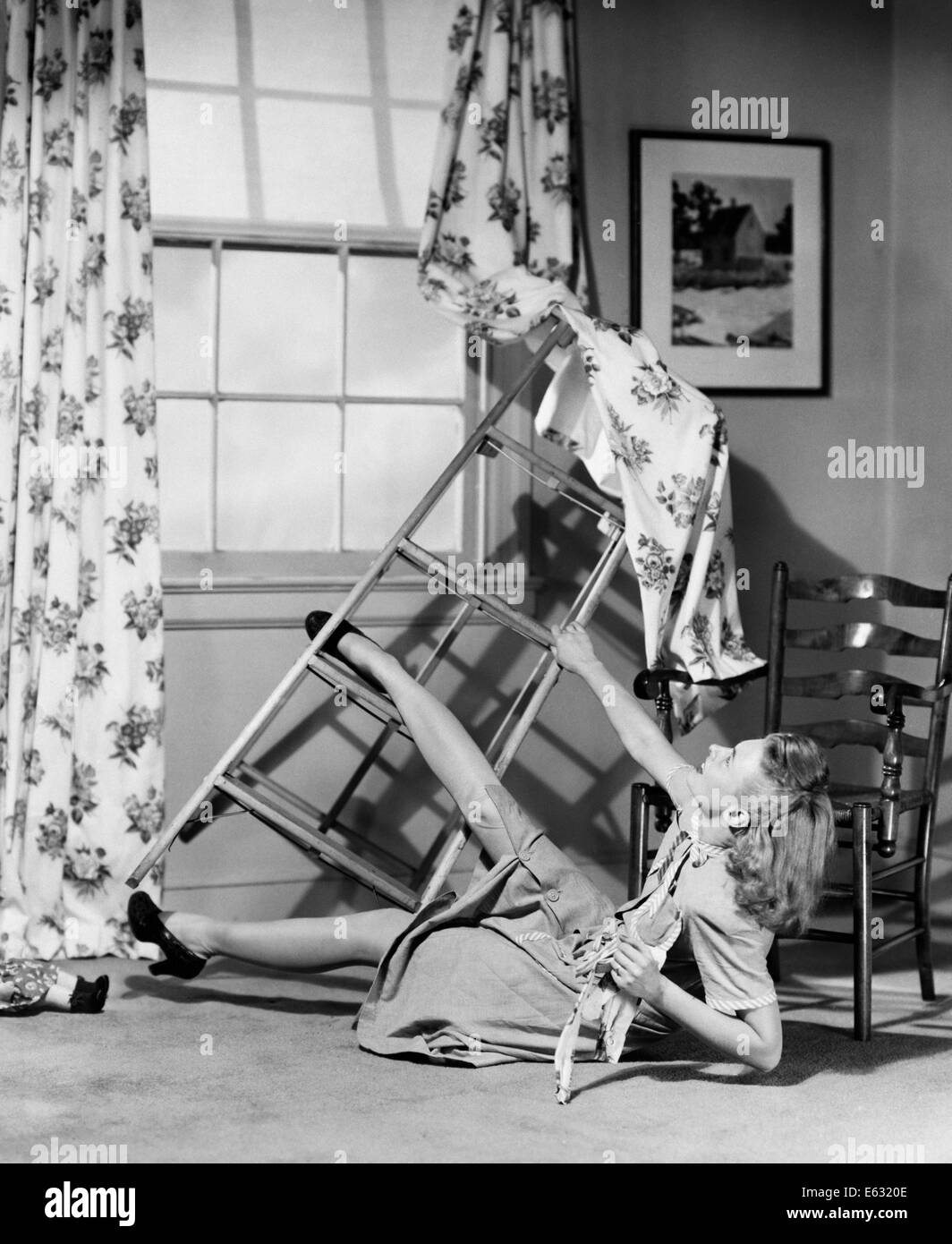 1940s 1950s WOMAN FALLING OFF OF STEP LADDER WHILE HANGING WINDOW CURTAINS Stock Photo