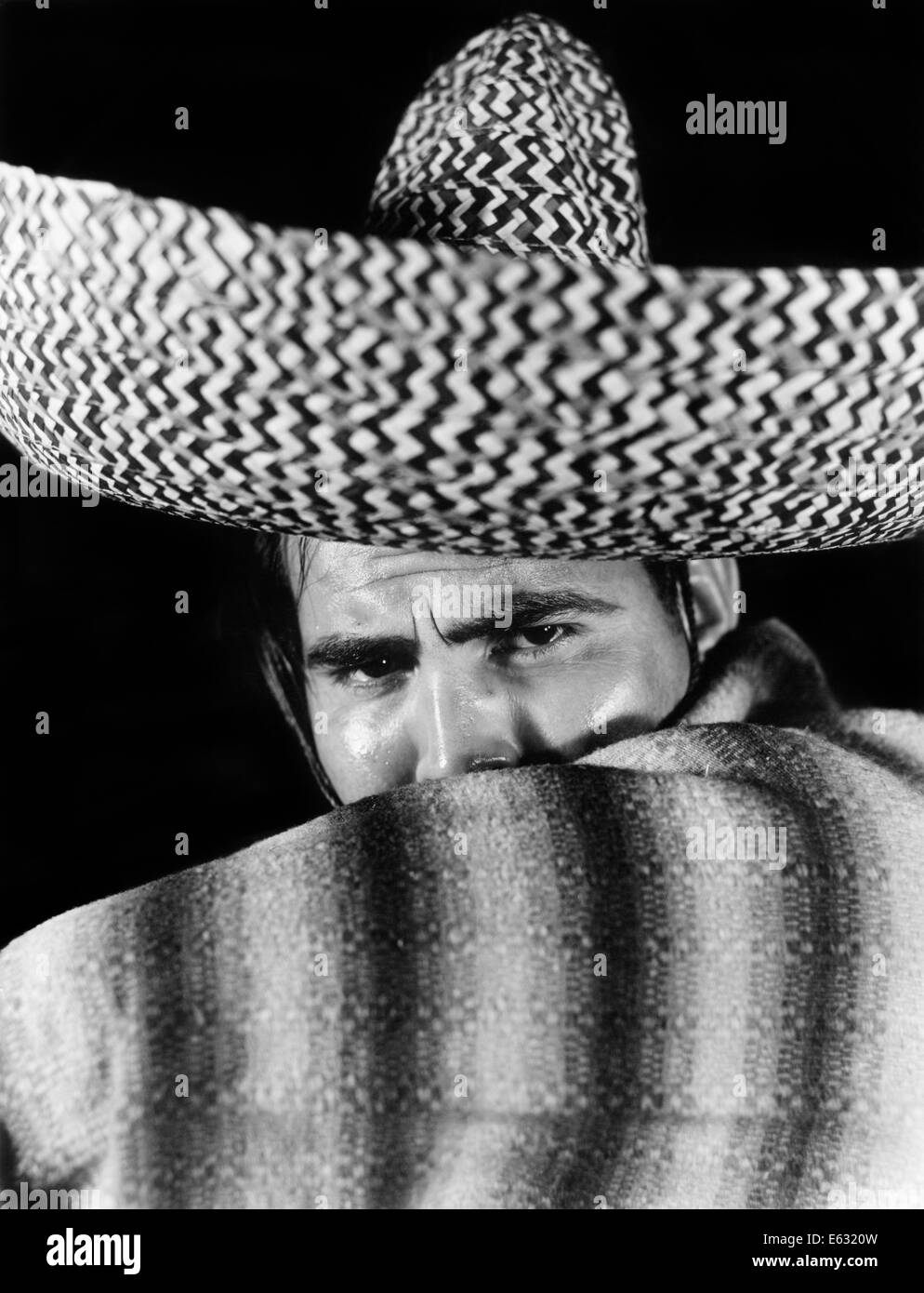1930s STEREOTYPE PORTRAIT MEXICAN MAN WEARING SOMBRERO HAT STRIPED BLANKET PONCHO COVERING MOUTH WITH ARM Stock Photo