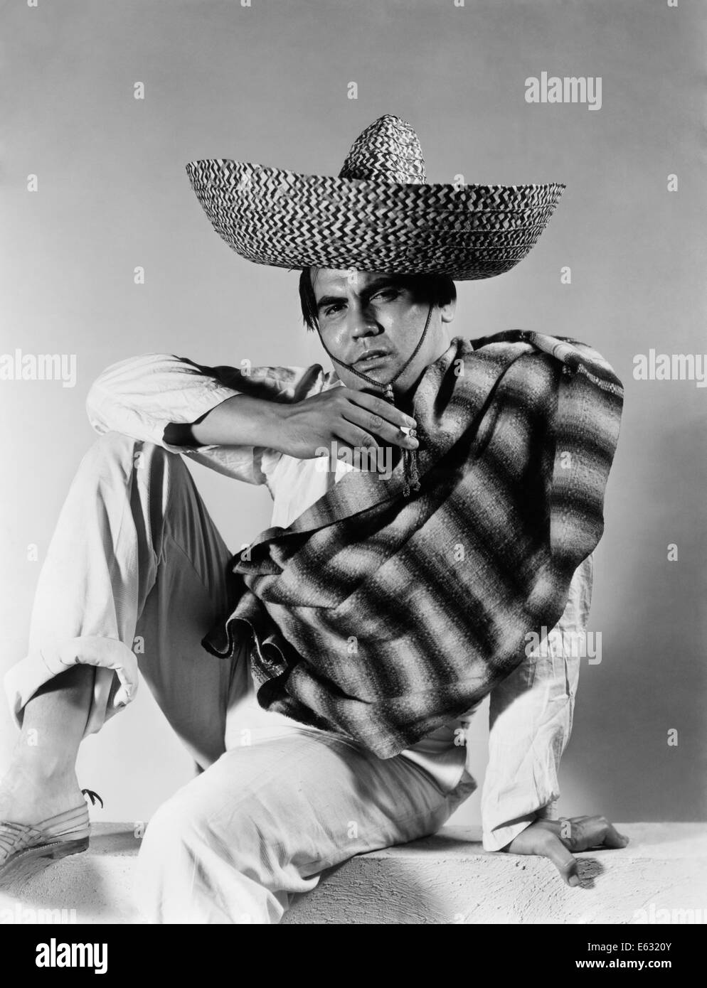 1930s 1940s STEREOTYPE PORTRAIT MEXICAN MAN WEARING STRIPED SERAPE SOMBRERO HAT SMOKING CIGARETTE Stock Photo