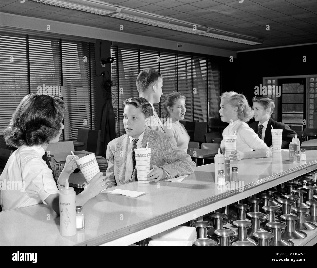 1950s YOUNG TEENAGE GIRLS AND BOYS DRINKING MILKSHAKES SITTING AT SODA FOUNTAIN COUNTER Stock Photo
