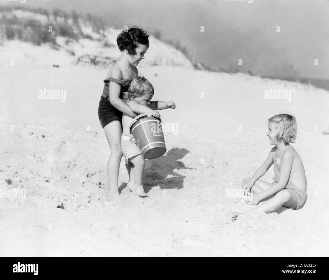 1930s THREE CHILDREN PLAYING IN SAND BEACH DUNES GIRLS TODDLER BUCKET  SUMMER FUN SEASHORE Stock Photo - Alamy