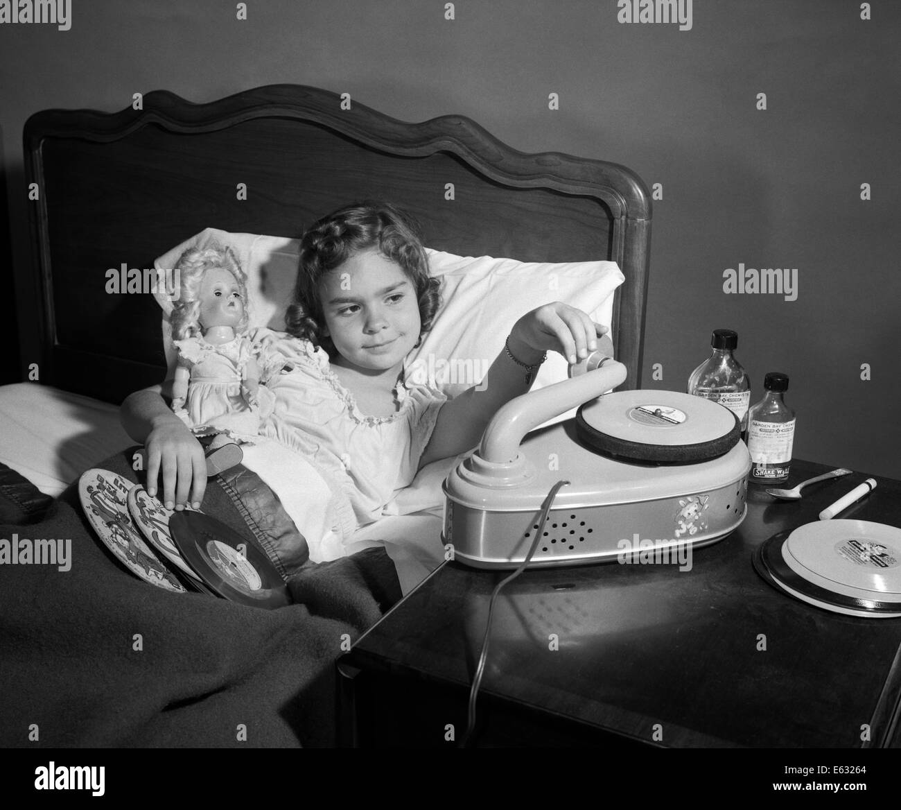 1950s GIRL SICK IN BED PLAYING RECORDS HOLDING BABY DOLL Stock Photo
