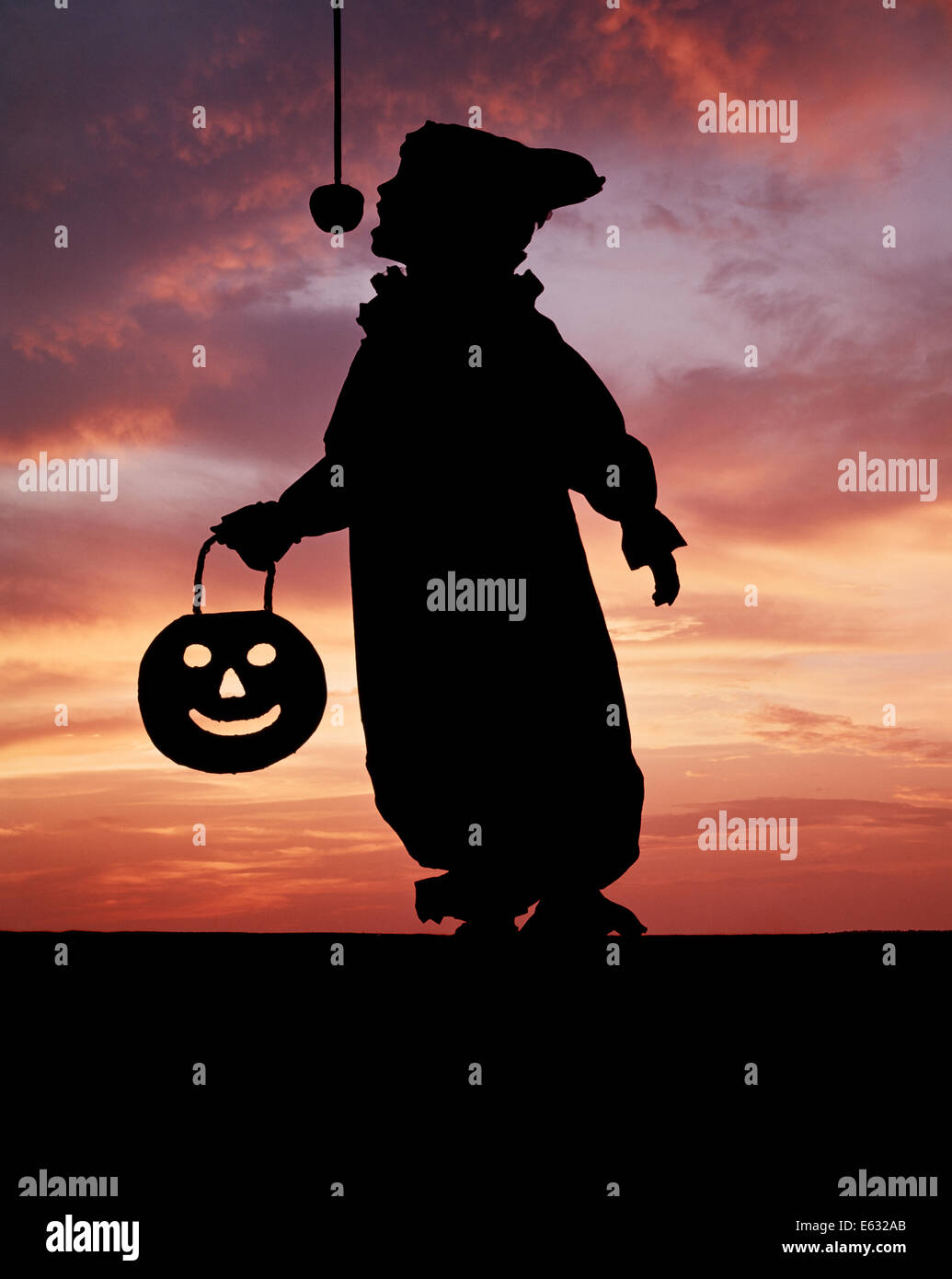 1970s SILHOUETTE OF CHILD CLOWN COSTUME CARRYING PUMPKIN FACE TRYING TO BITE APPLE SWINGING ON STRING Stock Photo