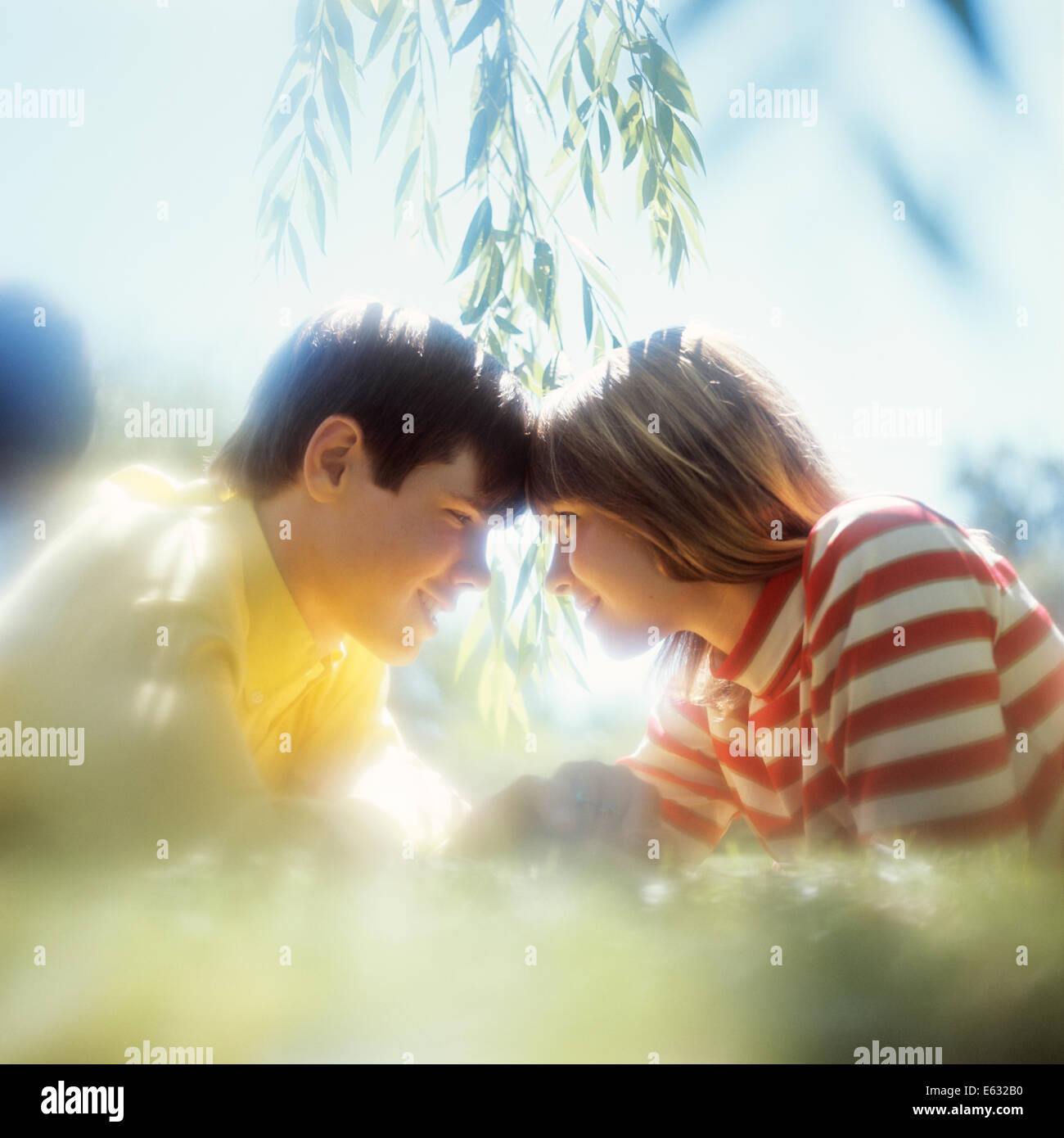 1970s TEENAGE BOY AND GIRL COUPLE LYING IN THE GRASS HEAD TO HEAD ROMANTIC SOFT FOCUS POSE Stock Photo