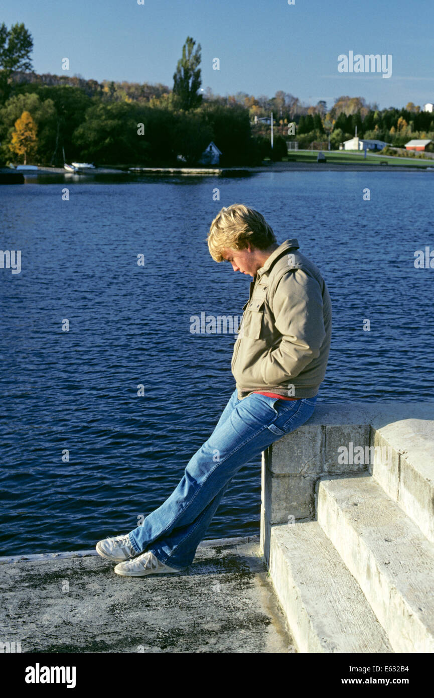 1980s INTROSPECTIVE TEENAGE BOY SITTING BY WATER Stock Photo