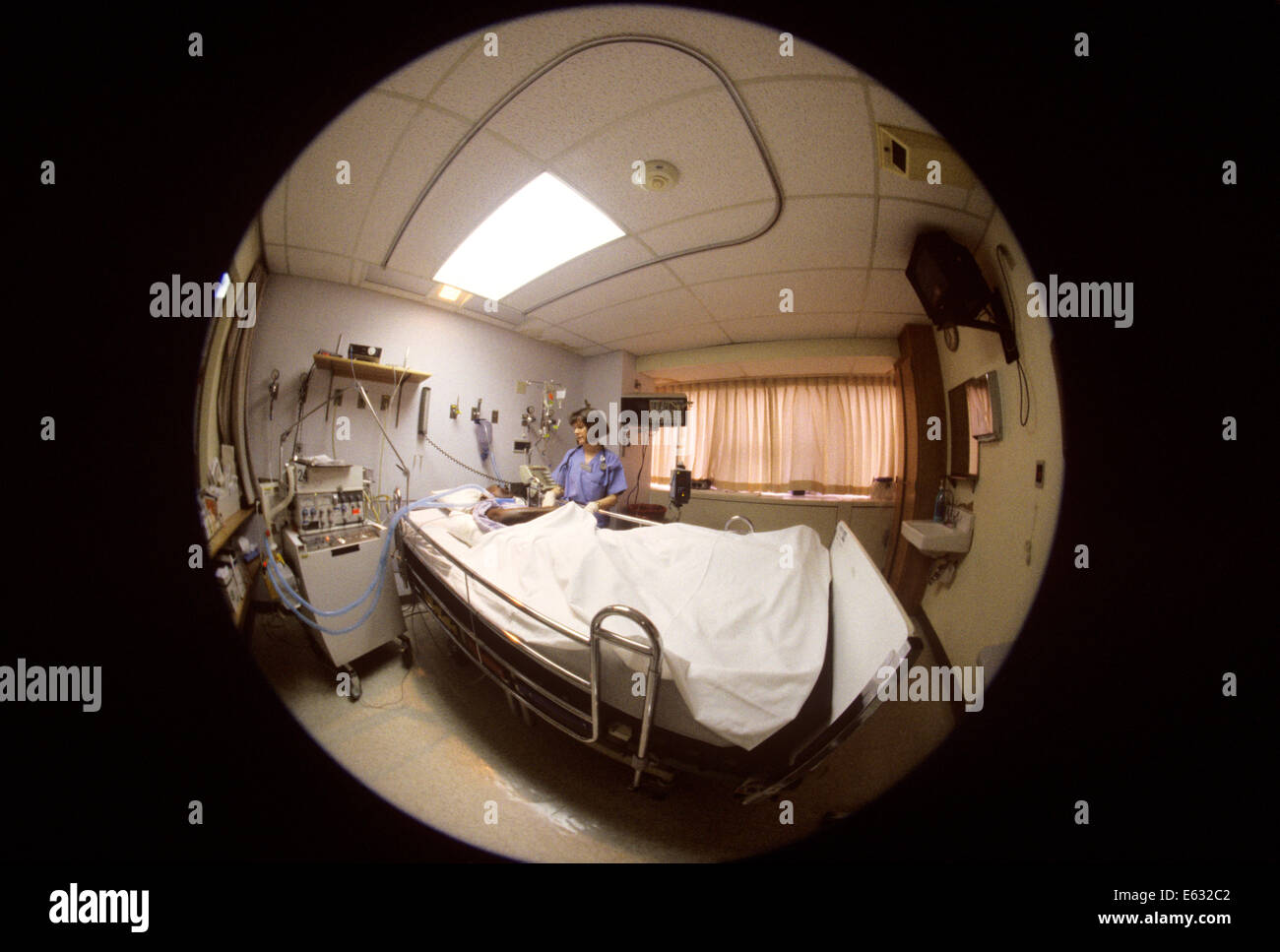 1990s FISHEYE LENS VIEW OF NURSE TENDING PATIENT IN INTENSIVE CARE UNIT ROOM Stock Photo