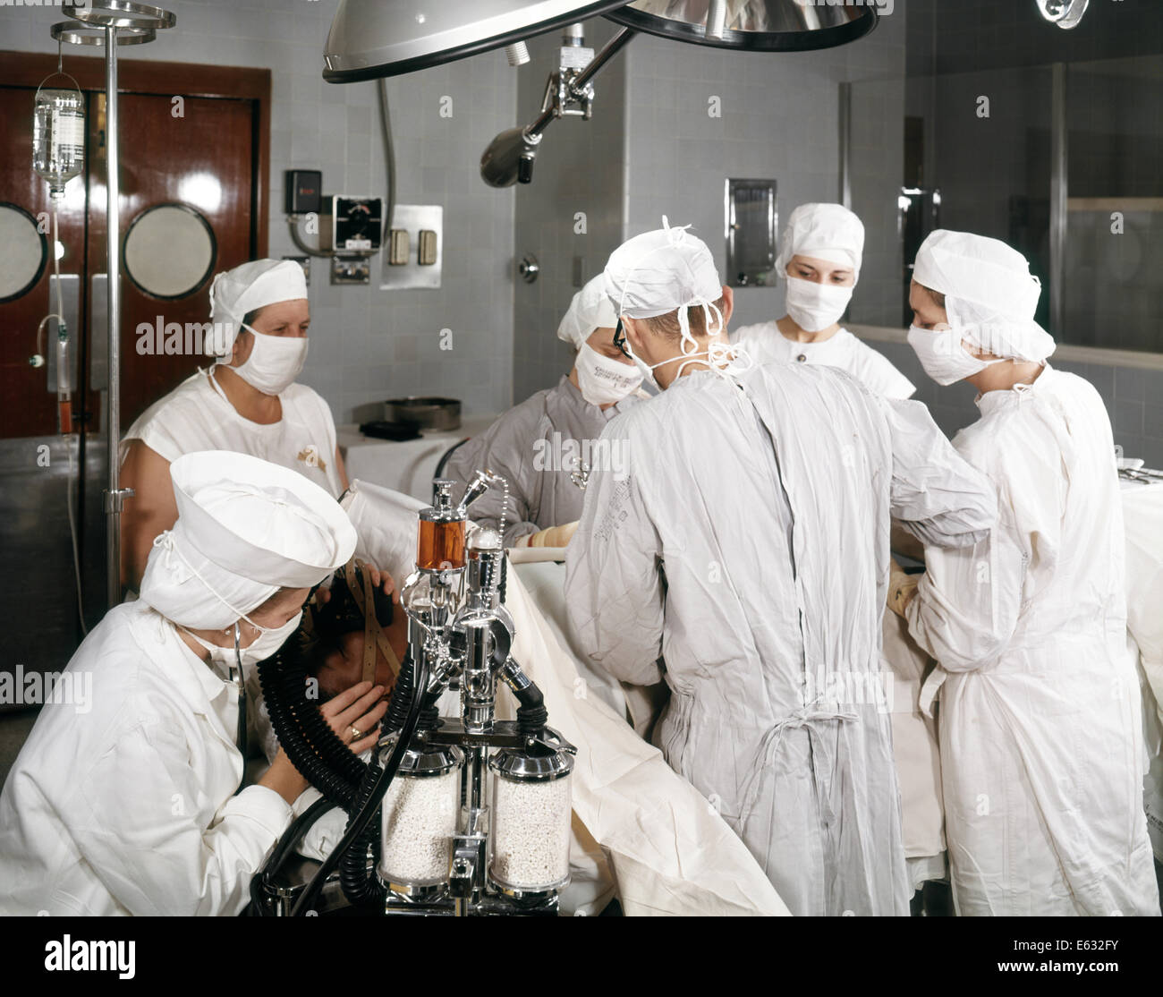 1960s OPERATING ROOM TEAM WITH SCRUB AND CIRCULATING NURSE TWO SURGEONS ANESTHETIST SUPERVISOR AND PATIENT Stock Photo