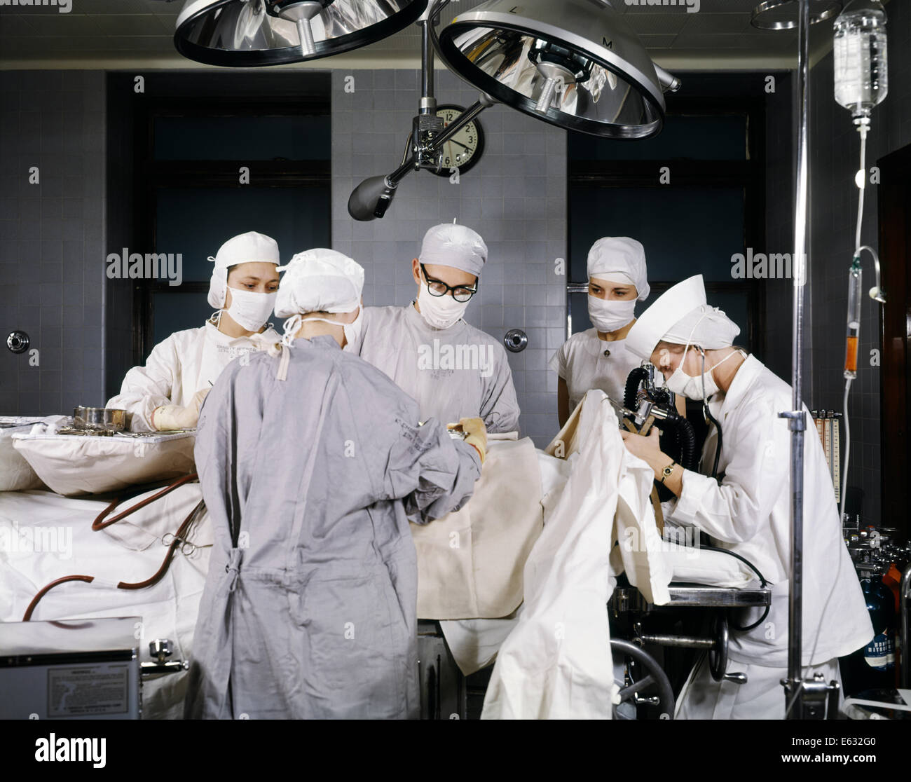 1950s HOSPITAL OPERATING ROOM SURGERY IN PROGRESS MEN WOMEN DOCTORS NURSES WEARING STERILE SURGICAL MASKS CAPS GOWNS Stock Photo