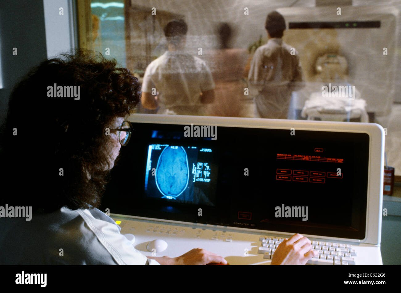 1980s FEMALE MEDICAL TECHNICIAN MONITORING CONSOLE FOR NUCLEAR MAGNETIC RESONANCE SCANNER Stock Photo