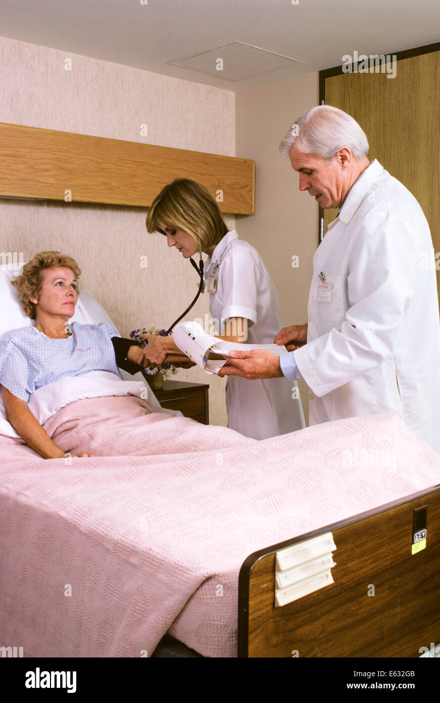 MATURE FEMALE PATIENT IN HOSPITAL BED NURSE AND DOCTOR TAKING VITALS VISITING Stock Photo