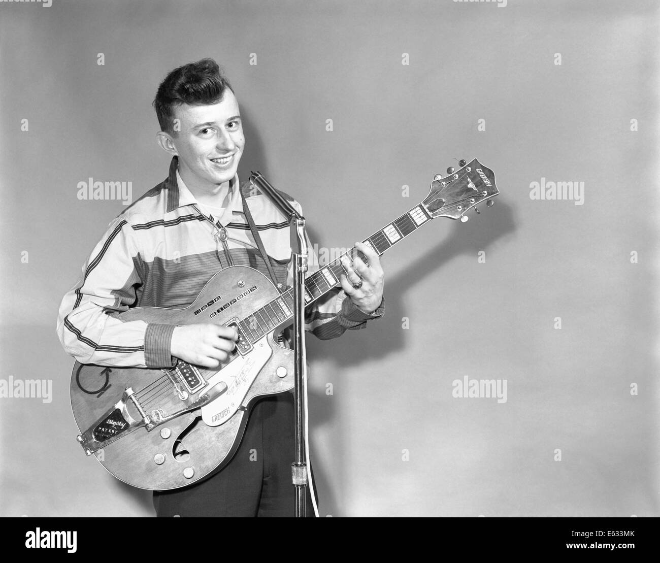 1950s TEENAGE BOY SINGING PLAYING GUITAR INTO MICROPHONE Stock Photo