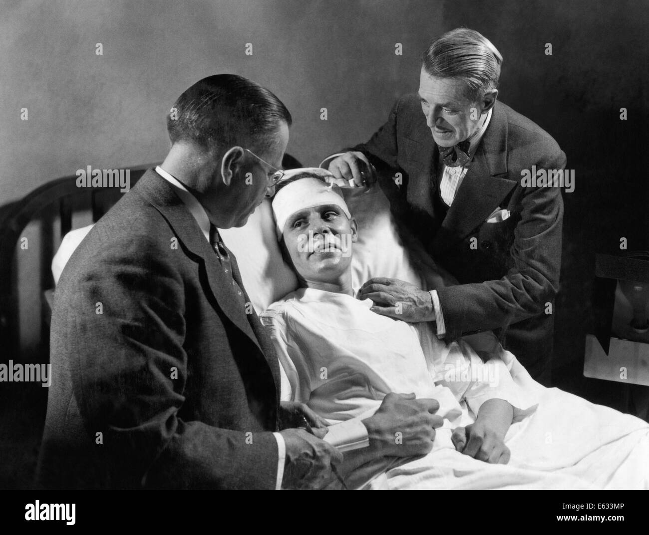1940s MALE PATIENT HOSPITAL BED HEAD WRAPPED BANDAGE BEING ATTENDED TO BY TWO MEN DOCTORS Stock Photo