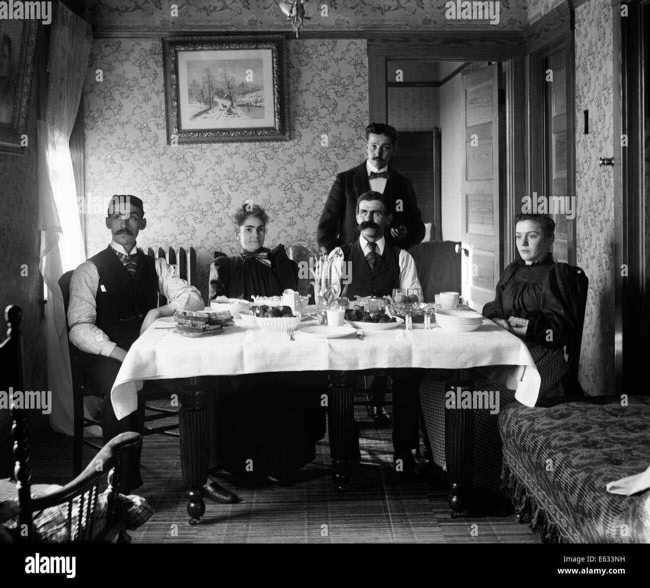 1890s THREE MEN TWO WOMEN FAMILY SITTING AT TABLE EATING MEAL Stock Photo