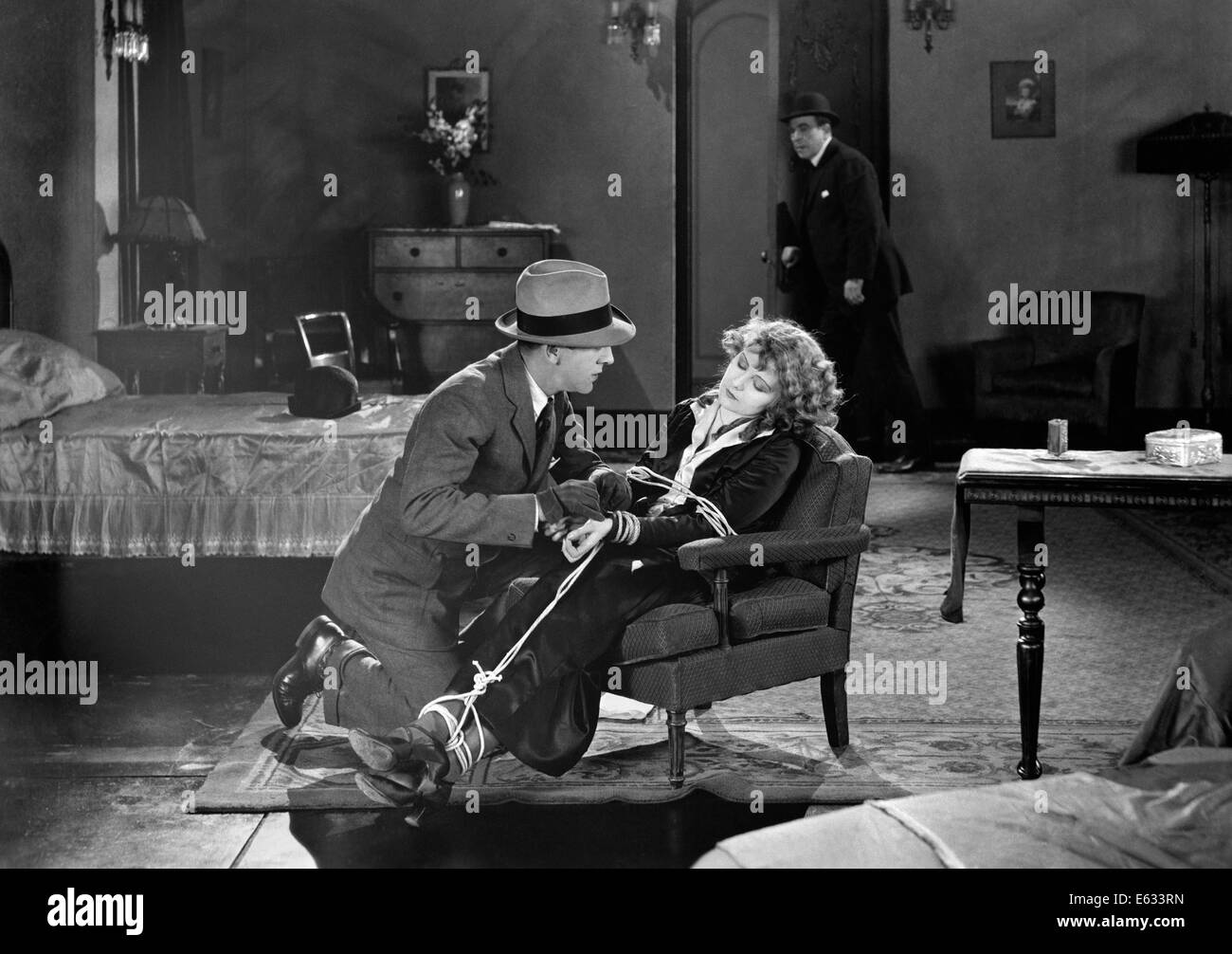 1930s MOVIE STILL OF MAN RESCUING WOMAN TIED UP IN CHAIR Stock Photo