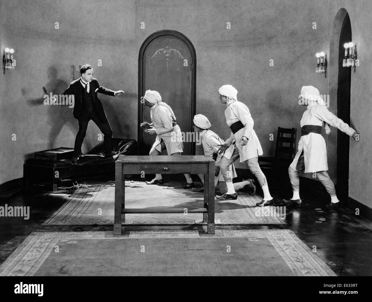 1920s MAN IN SUIT AND TIE BEING CHASED BY GANG OF THUGS WEARING TURBANS SILENT MOVIE STILL Stock Photo