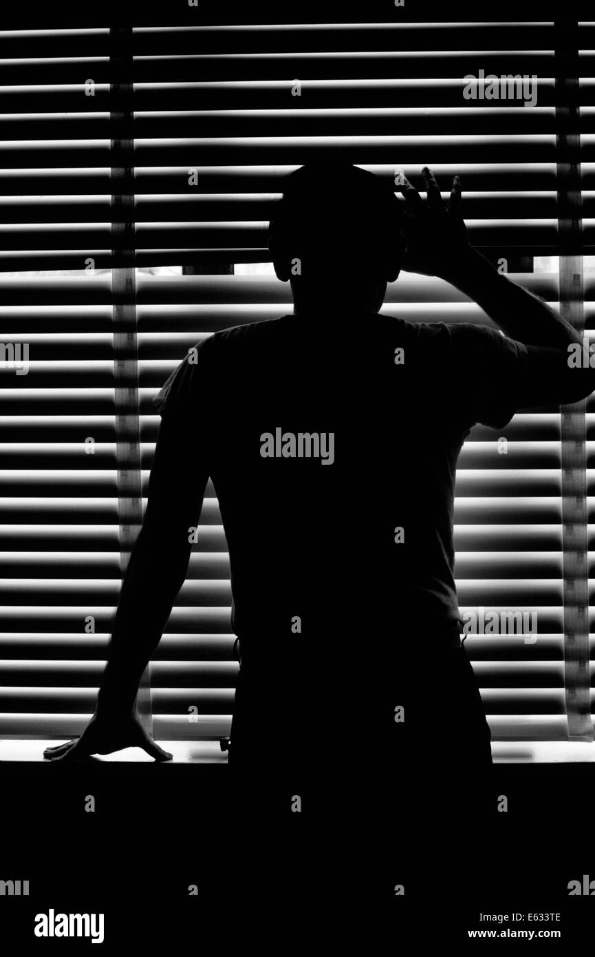 REAR VIEW SILHOUETTE OF ANONYMOUS MAN PEEKING THROUGH VENETIAN BLINDS Stock Photo