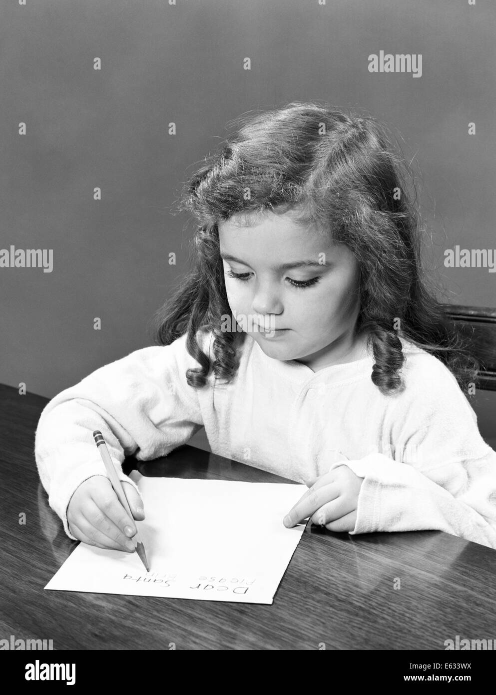 1940s LITTLE GIRL WITH CURLY HAIR WRITING LETTER WITH PENCIL AND PAPER Stock Photo