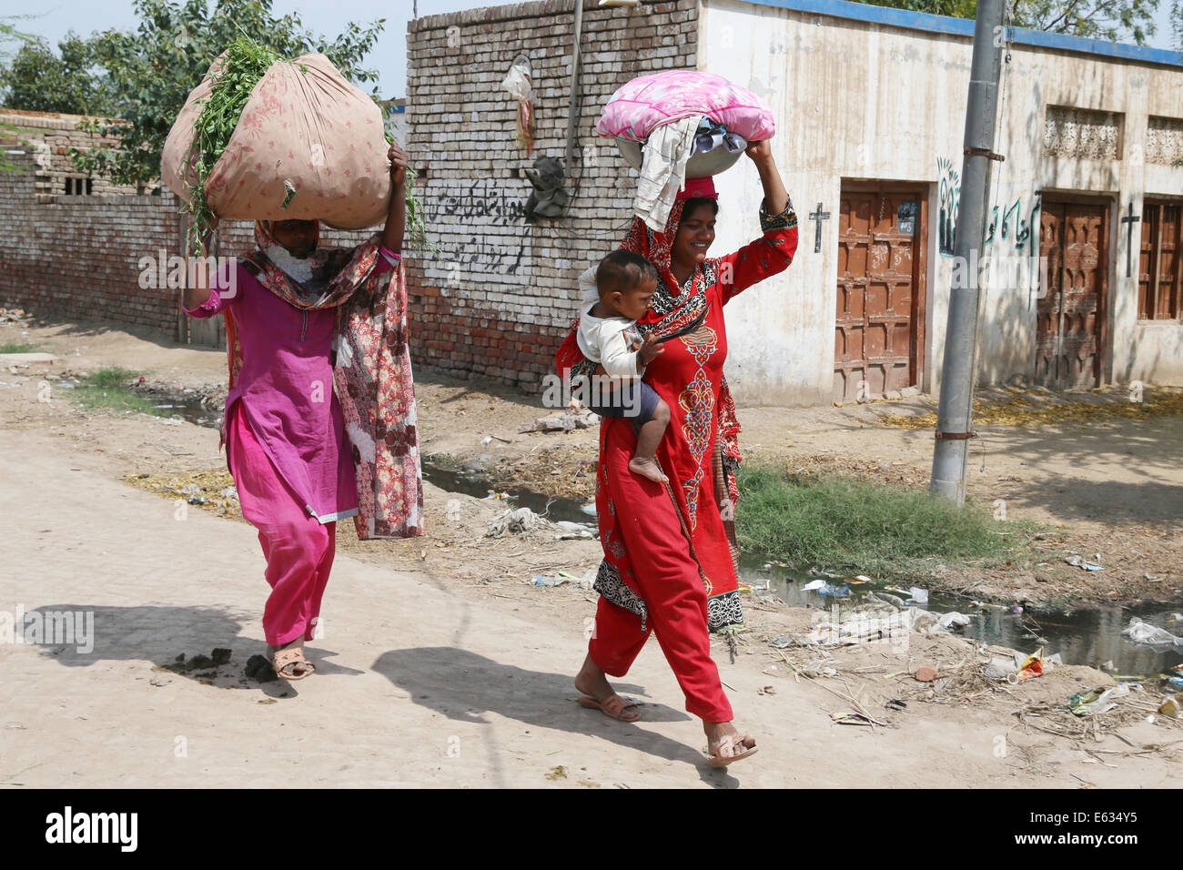 two women carry loads on their heads in the christian dominated village of Khushpur, Punjab province, Pakistan Stock Photo