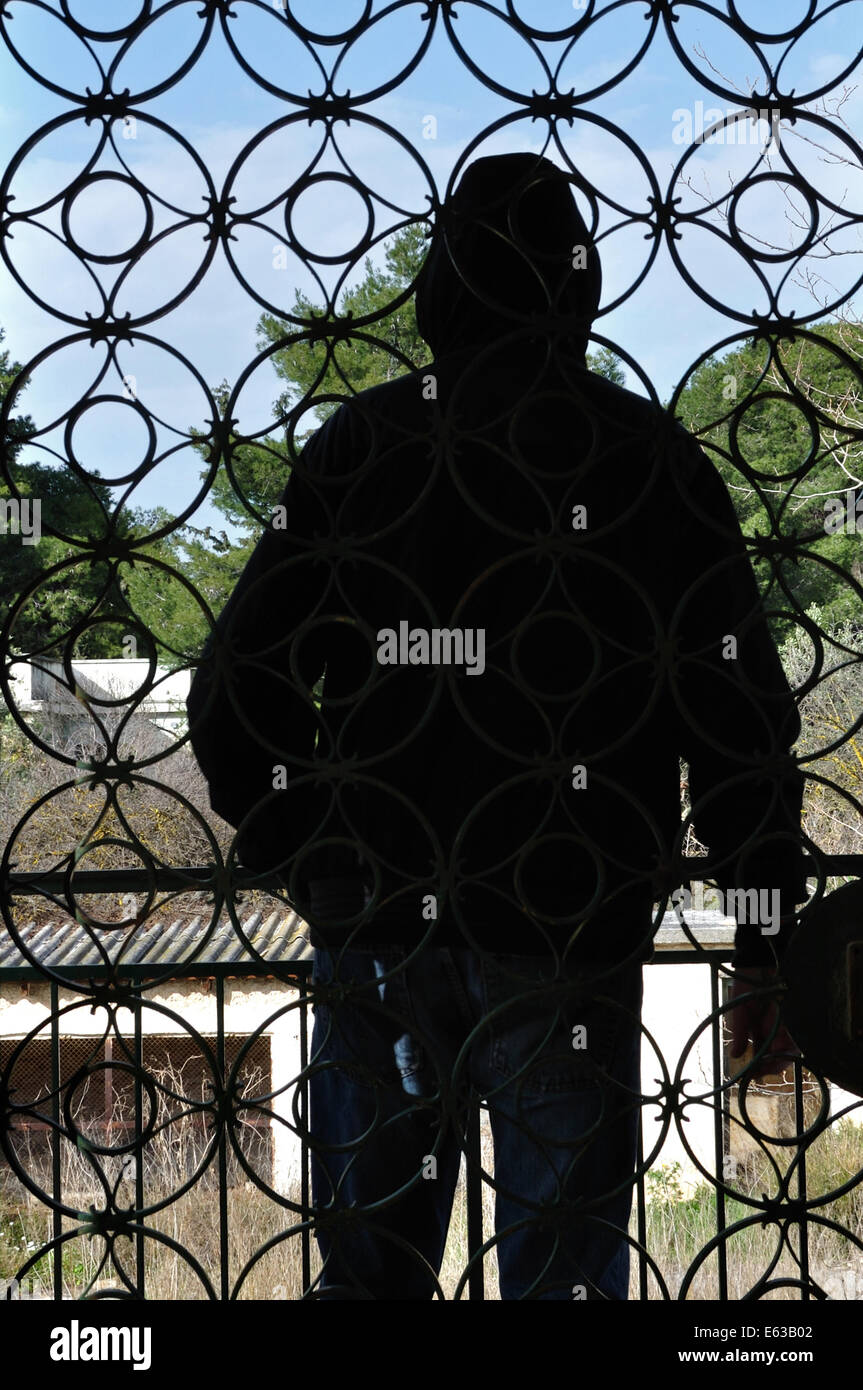 Hooded man looking at view from the balcony of an abandoned house and vintage iron gate circles pattern. Stock Photo
