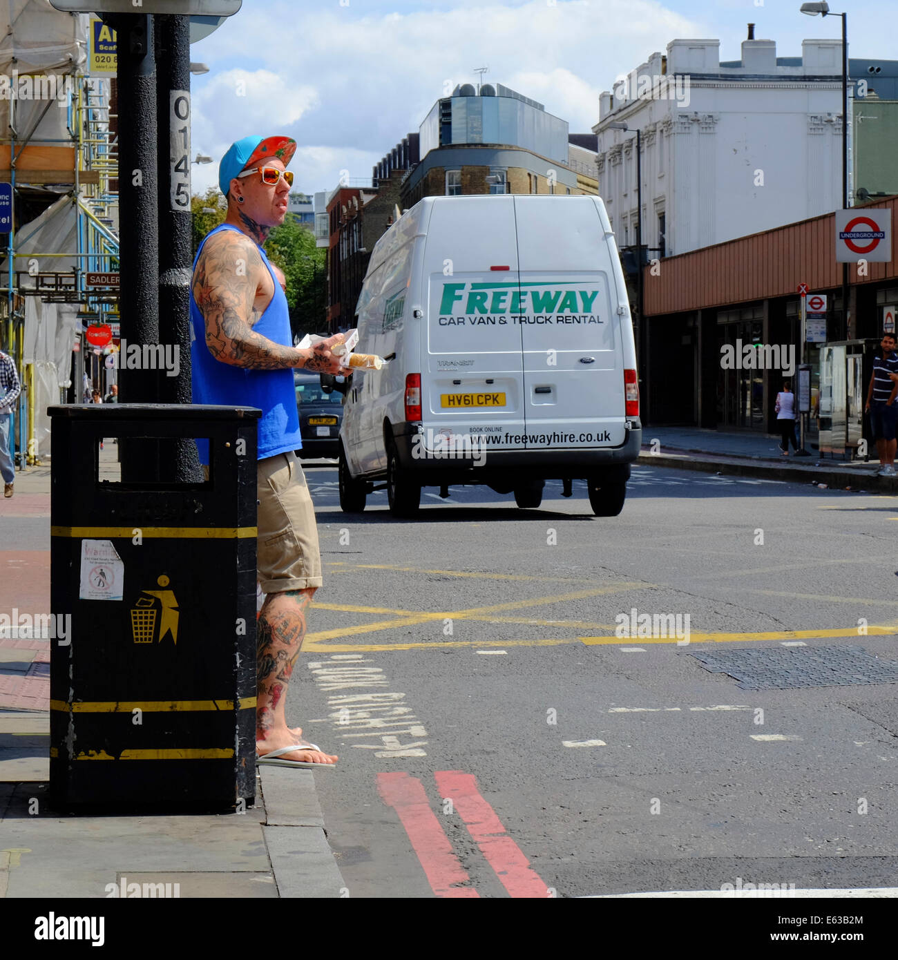 young man with tattoos carrying lunch, waiting to cross street in London Stock Photo