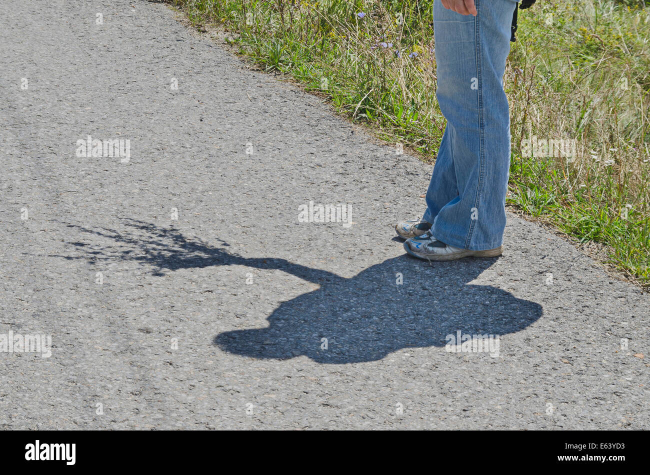 Legs of female tourist in sneakers and shadow on the mountain road Stock Photo
