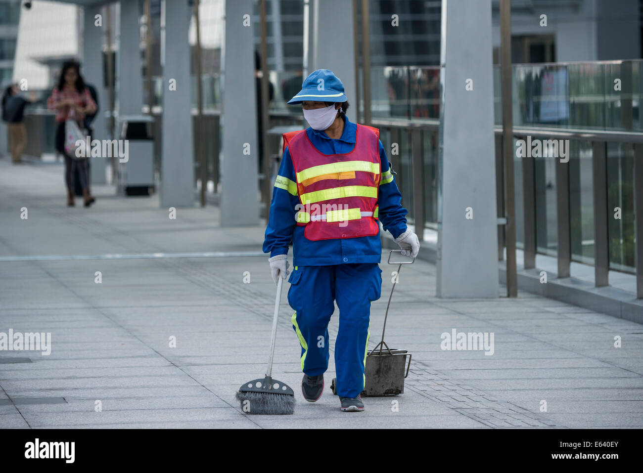 Female street cleaner wearing a safety vest, mask and holding a sweeping tool, Shanghai, China Stock Photo