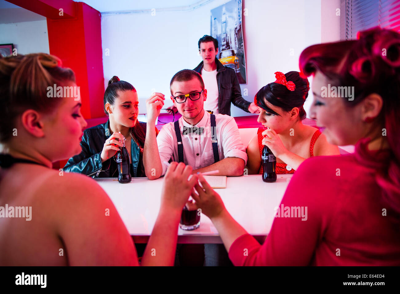 A geek geeky man dressed in 1950's style American clothing fashion in a diner with four women Stock Photo