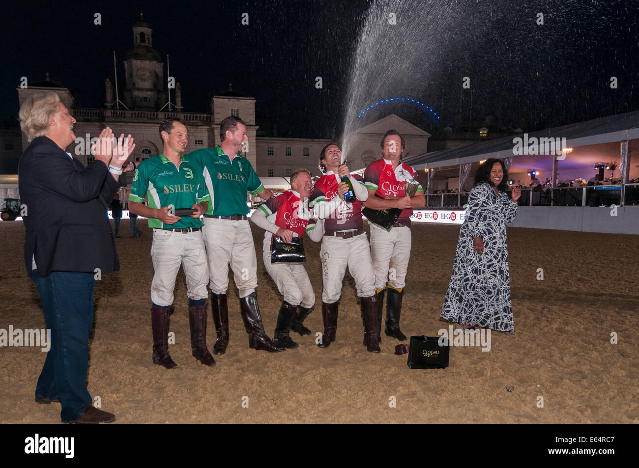 London, UK, 14 August 2014.  The famous Horse Guards Parade hosts City Polo, an inaugural evening of international arena polo.  Pictured : Team Wales celebrate with champagne after receiving their winner's trophy from designer, David Emanuel.   Credit:  Stephen Chung/Alamy Live News Stock Photo