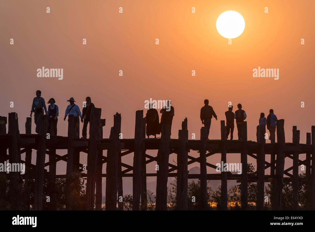 Locals, monks and tourists walking on a teak bridge, U Bein Bridge across Thaungthaman Lake at sunset, Amarapura Stock Photo