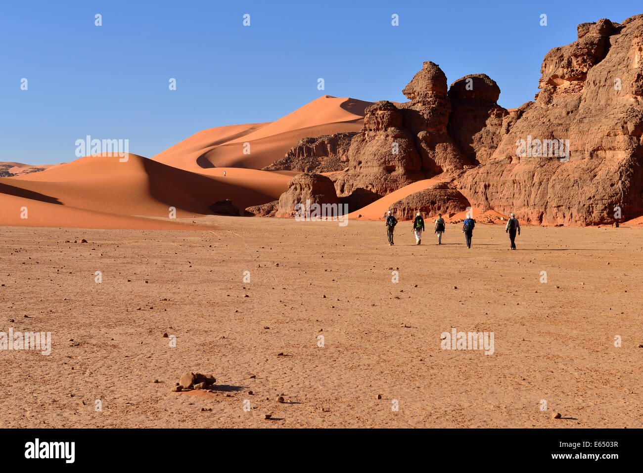 People hiking between rocks and sand dunes of Tin Merzouga, Tadrart ...