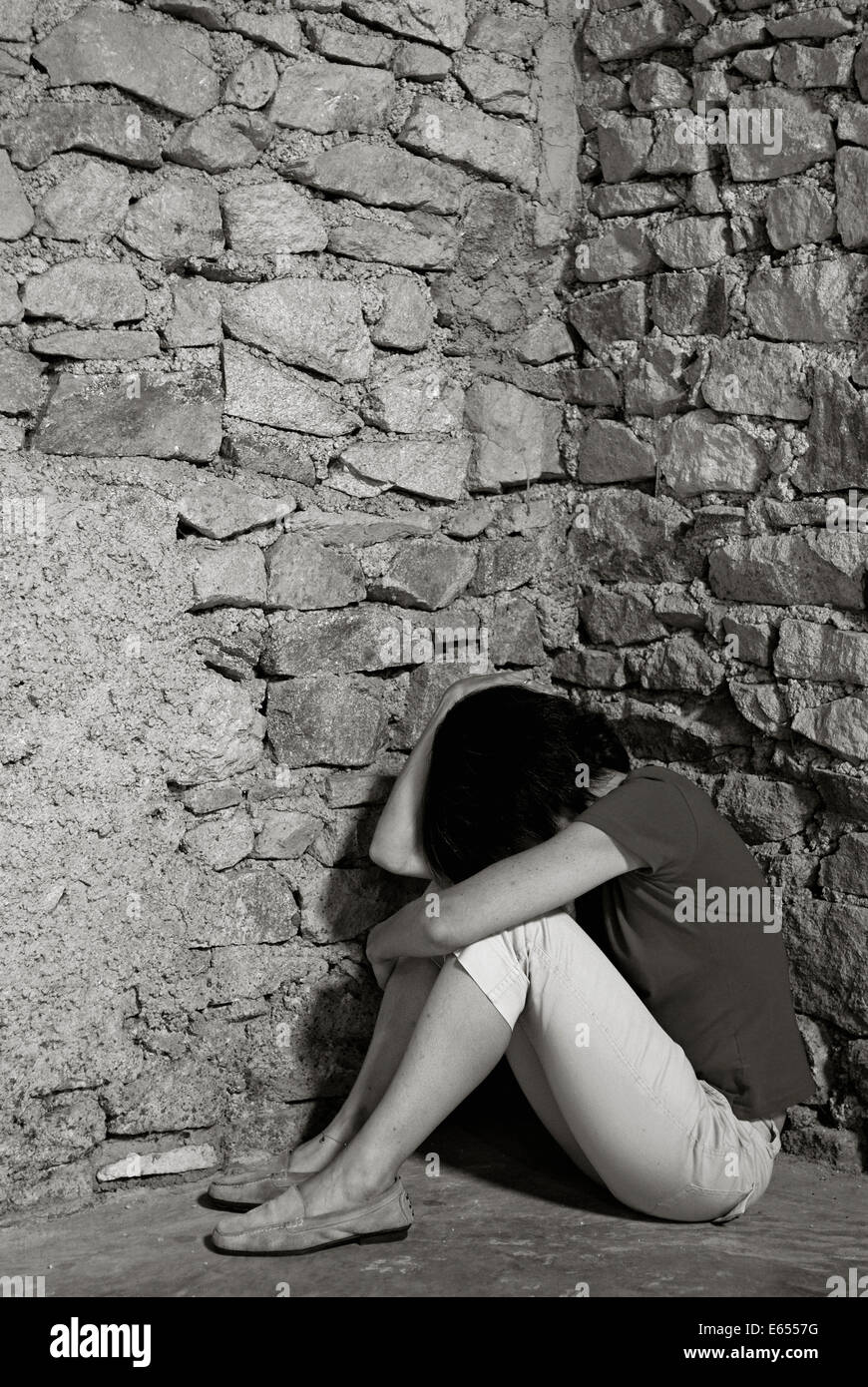 Depressed middle-aged woman sitting with head in hands in a room corner Stock Photo