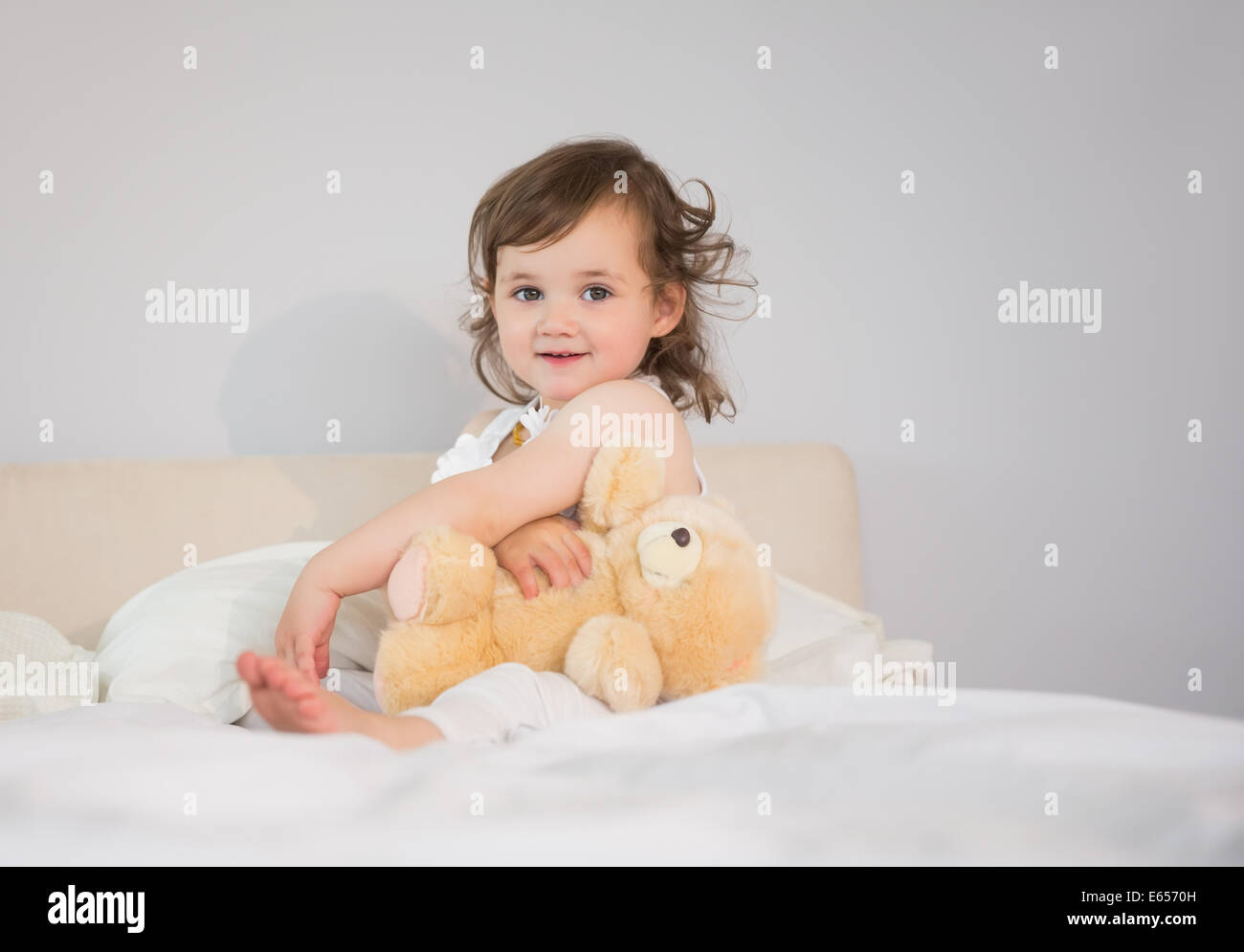Portrait of cute little girl sitting on bed Stock Photo - Alamy