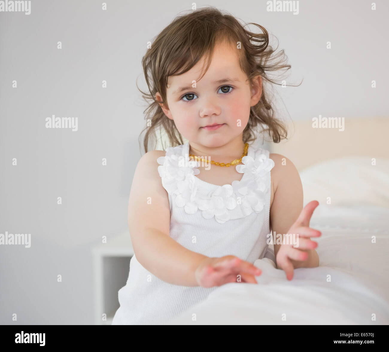 Portrait of cute little girl sitting on bed Stock Photo - Alamy