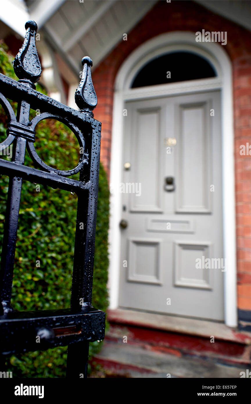 An open front gate leading to a hedge and grey front door of a terraced victorian house. Stock Photo