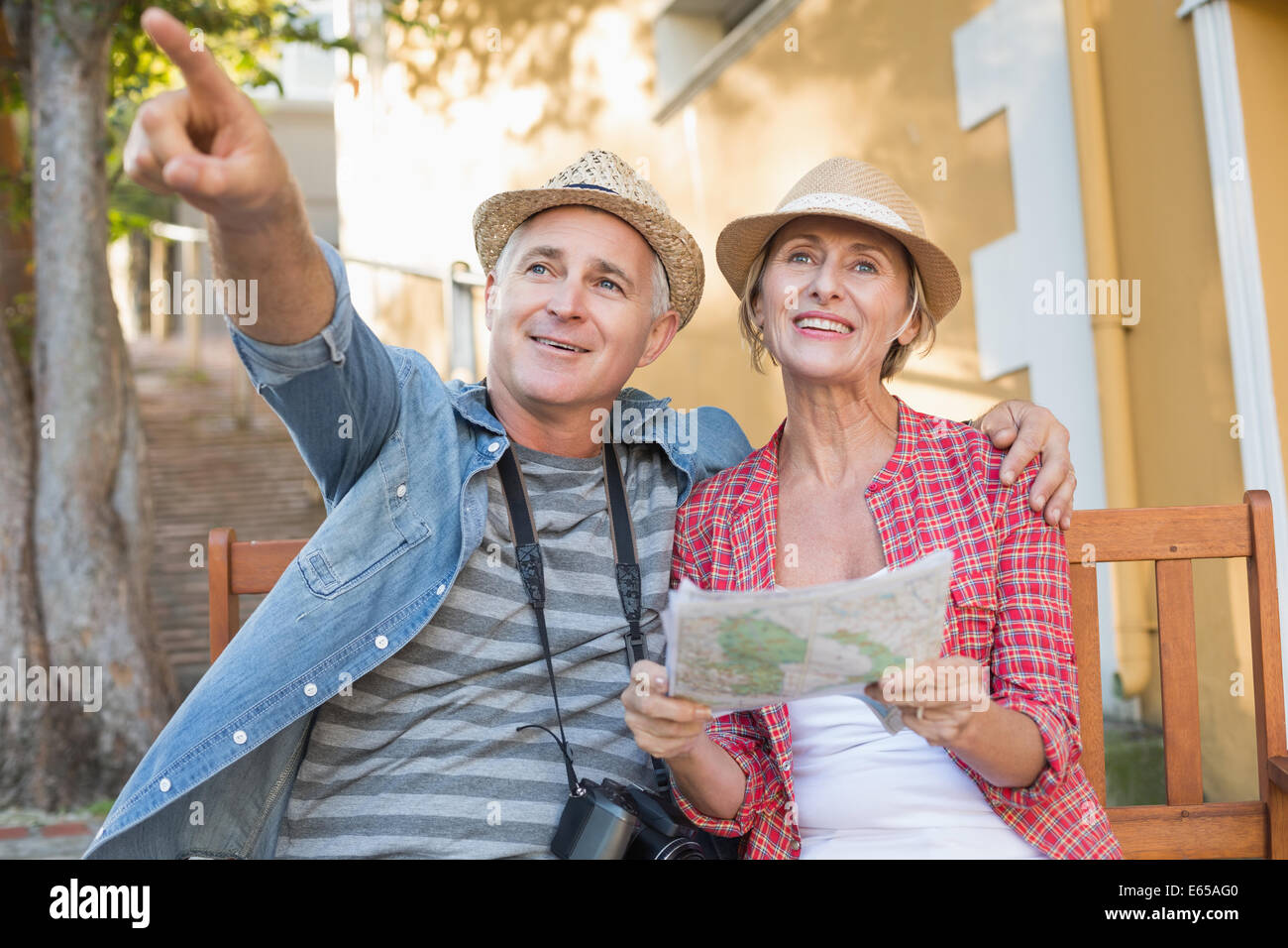 Happy tourist couple looking at map on a bench in the city Stock Photo