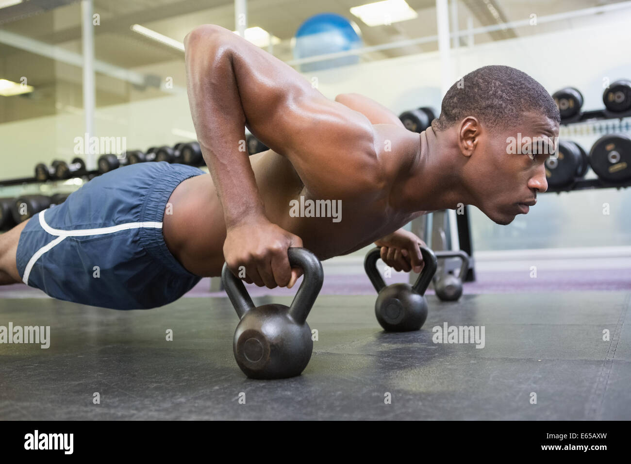 Determined man doing push ups with kettle bells in gym Stock Photo