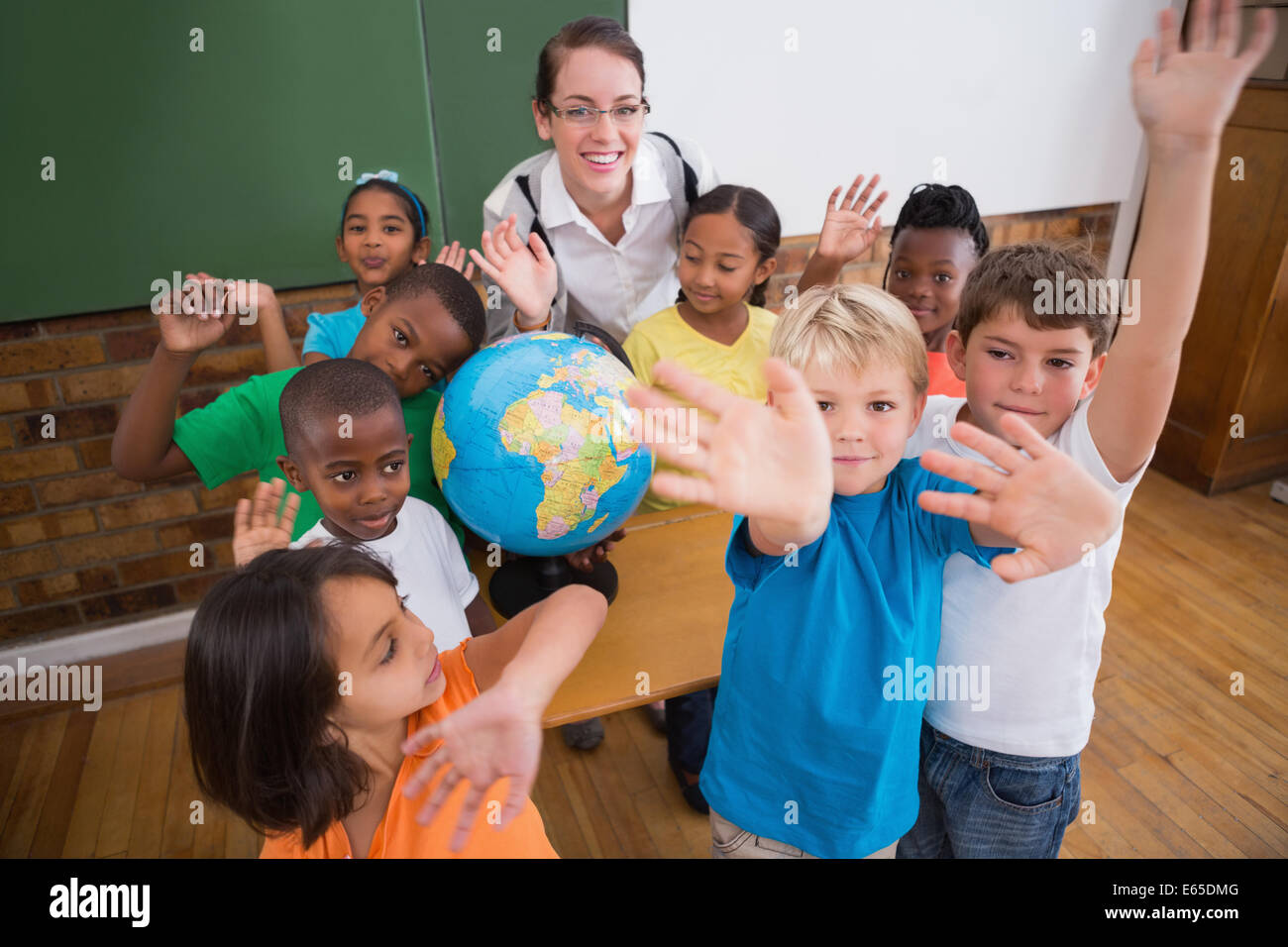 Cute pupils smiling around a globe in classroom with teacher Stock ...