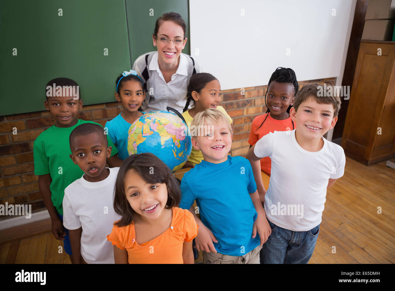 Cute pupils smiling around a globe in classroom with teacher Stock ...