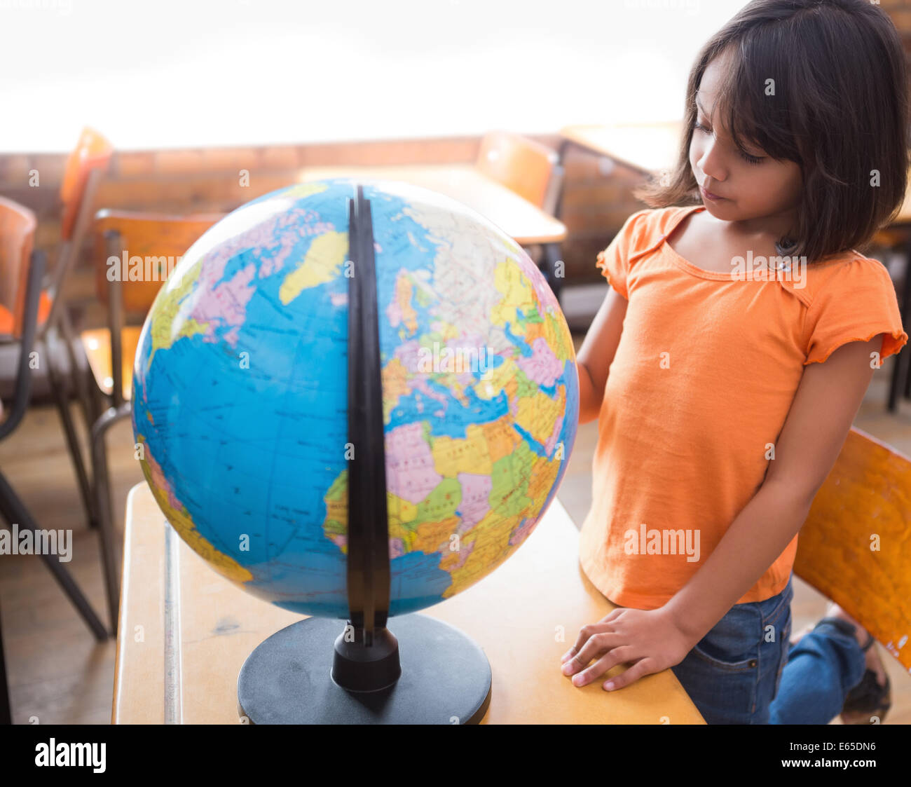 Cute little pupil looking at globe in classroom Stock Photo - Alamy